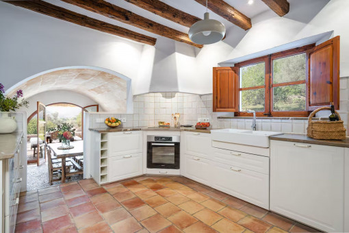 Bright country-style kitchen with wooden beams, terracotta floor and view into the dining room with access to the terrace